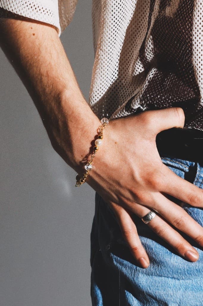 Gold and pearl bracelet on a wrist with a hand tucked into light-wash denim