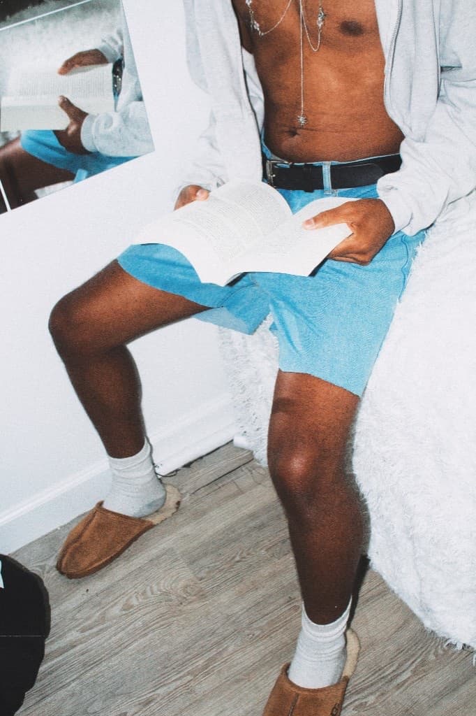 Candid frame reading a book in denim shorts and slippers wearing the silver necklace